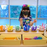 Young girl in school choosing color pens, wearing mask in the time of COVID-19