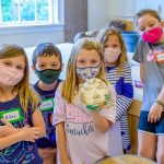 Children in school photography showing pottery mask sculpture, masked in time of COVID-19