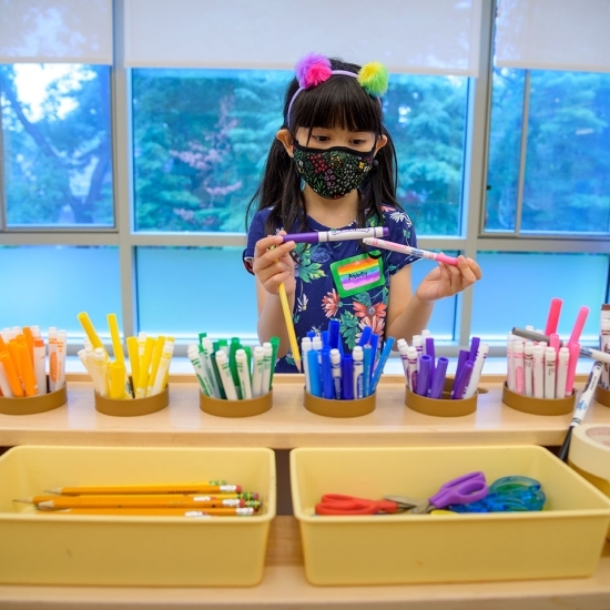 Photo of young girl in school choosing color pens, wearing mask in the time of COVID-19